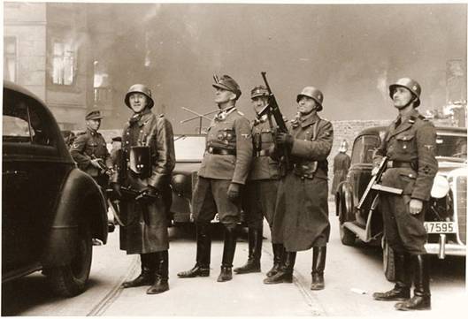 Generál SS Jürgen Stroop (druhý muž zleva s polní čepicí) a jeho muži pozorují hořící domy ve varšavském ghettu